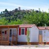 Due case mobili bianche con persiane rosse tra gli alberi, una collina con edifici sullo sfondo.