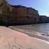 Una spiaggia sabbiosa con onde leggere e alte scogliere rocciose al sole.