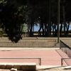 Campo da tennis all'aperto, circondato da alberi e panchine.