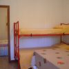 Letto a castello rosso con coperte gialle accanto a un tavolo con tovaglia a fiori, pareti bianche.