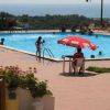 Piscina all'aperto con bagnanti, ombrellone rosso e vista mare.
