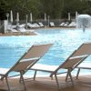 Piscina all'aperto con lettini inclinati sul bordo in legno e un fungo d'acqua centrale.