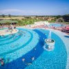 Grande piscina a onde con persone che nuotano e fontana centrale.