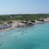 Spiaggia affollata con acqua cristallina e ombrelloni blu.