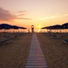 Spiaggia al tramonto con ombrelloni e lettini blu.