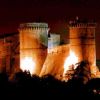 Un castello medievale illuminato di notte, con torri robuste e mura imponenti.