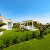 Giardino con prato verde, pergola bianca e vista mare, cielo sereno.