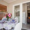 Tavolo da pranzo con tovaglia floreale, fiori e piatti, vicino a una cucina con frigorifero.